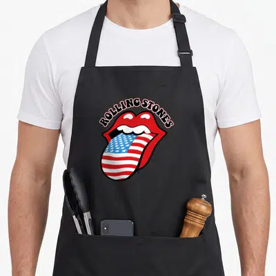 Vintage tongue rolling stones apron - Red mouth with tongue filled in USA flag pattern under arched text — shown on a black cotton canvas apron against a white background