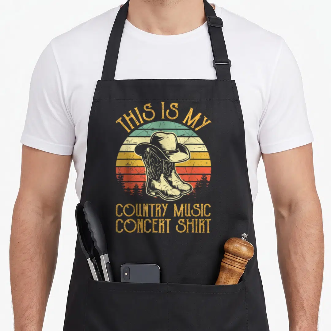 Music country kitchen apron - Retro cowboy boots and hat over striped sun with text THIS IS MY COUNTRY MUSIC CONCERT — shown on a black cotton canvas apron against a white background