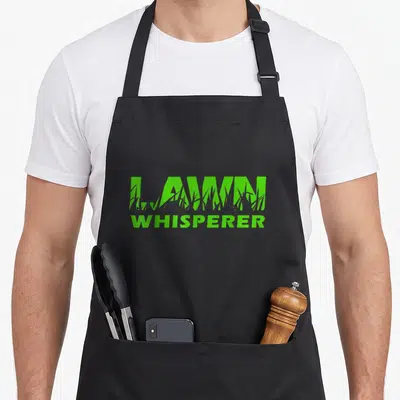 Whisperer yard work apron - Green stacked text LAWN WHISPERER with grass blades cutting through the top word — shown on a black cotton canvas apron against a white background