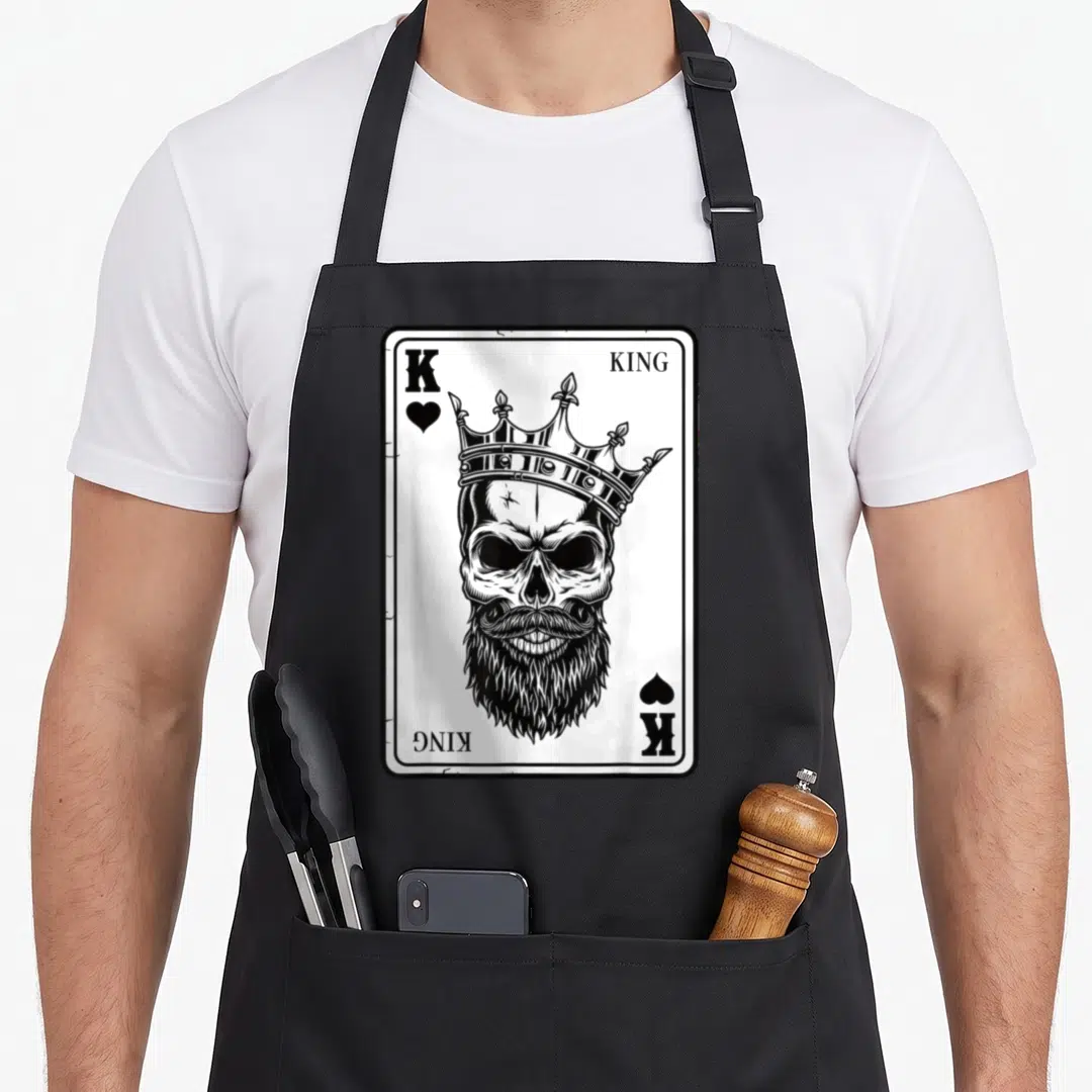 King couple apron - Crowned bearded skull on playing card with K and KING text in black and white — shown on a black cotton canvas apron against a white background