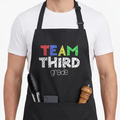 Third alumni squad apron - Stacked text reading TEAM THIRD grade in red blue yellow green and white sketch fonts — shown on a black cotton canvas apron against a white background