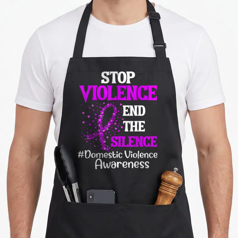Silence domestic aprons - STOP VIOLENCE END THE SILENCE text with magenta heart ribbon and hashtag — shown on a black cotton canvas apron against a white background