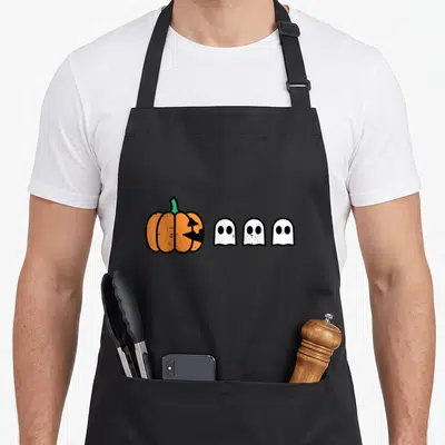 Gamer pumpkin halloween apron - Cartoon orange pumpkin with bite marks facing three white ghosts in black outline — shown on a black cotton canvas apron against a white background
