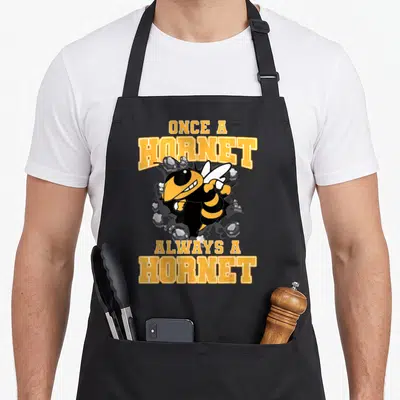 Alway school apron - Cartoon hornet bursting through rocks with Once a Hornet Always a Hornet text — shown on a black cotton canvas apron against a white background