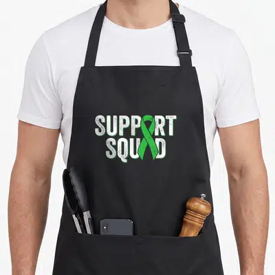 Kidney disease ribbon apron - Vertical green ribbon overlapping white SUPPORT SQUAD text in distressed font — shown on a black cotton canvas apron against a white background