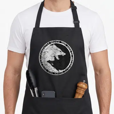 Fenrir nordic apron - Circular distressed wolf head in yin-yang style with runic text border — shown on a black cotton canvas apron against a white background