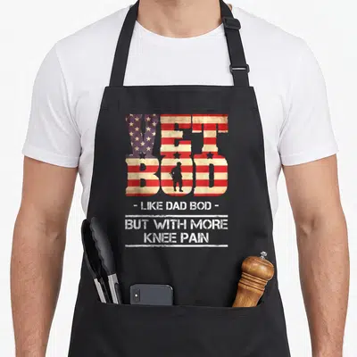 Vet dad bod apron - VET BOD flag text with soldier silhouette and knee pain quote in distressed red white blue — shown on a black cotton canvas apron against a white background