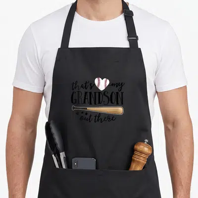 Retro grandson grandma apron - Heart shaped baseball and tan bat under black text that's my GRANDSON out there — shown on a black cotton canvas apron against a white background