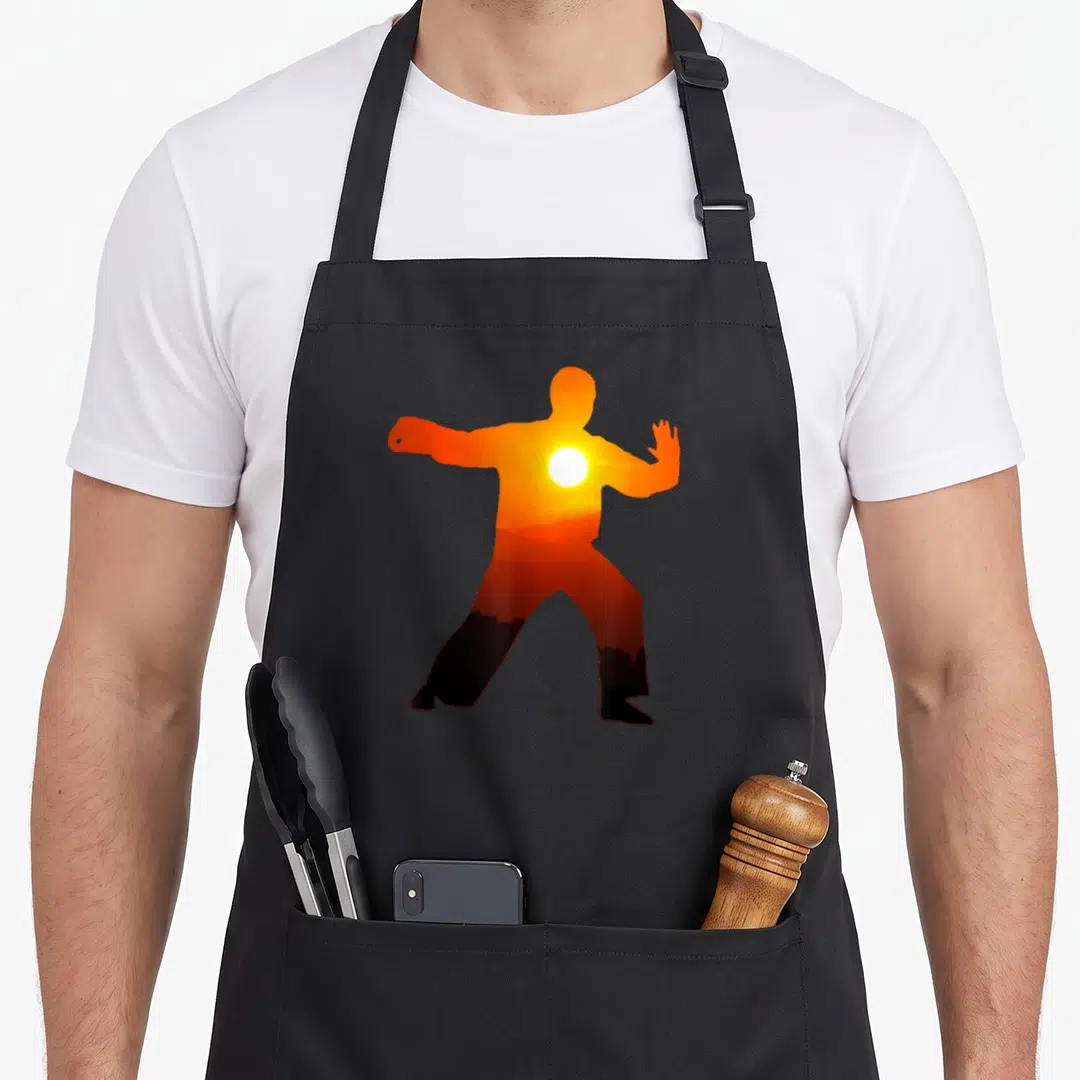 Chi qigong apron - Martial arts silhouette filled with orange sunset and mountain landscape in minimalist style — shown on a black cotton canvas apron against a white background