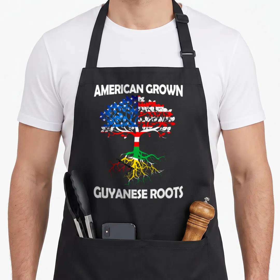 Grown guyana apron - Tree with US flag leaves and Guyanese roots flanked by American Grown Guyanese Roots text — shown on a black cotton canvas apron against a white background