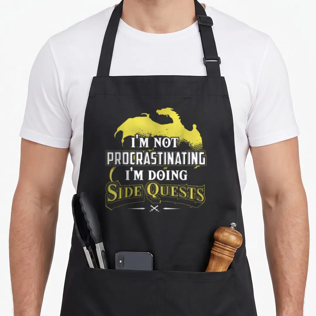 Rpg crew apron - Yellow dragon silhouette with white text I'm not procrastinating I'm doing side quests and two crossed — shown on a black cotton canvas apron against a white background