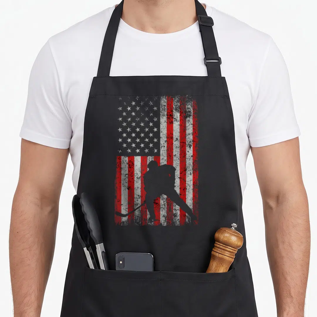 Ice american flag apron - Grey hockey player silhouette over distressed red white and grey US flag pattern — shown on a black cotton canvas apron against a white background