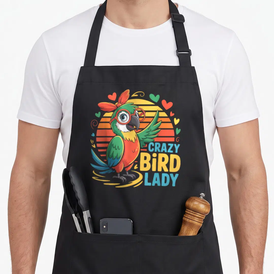 Retro parrot bird apron - Cartoon parrot with glasses next to CRAZY BIRD LADY text on striped sun background — shown on a black cotton canvas apron against a white background