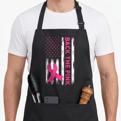 Retro breast cancer awareness aprons - Pink ribbon over distressed US flag with vertical BACK THE PINK text — shown on a black cotton canvas apron against a white background
