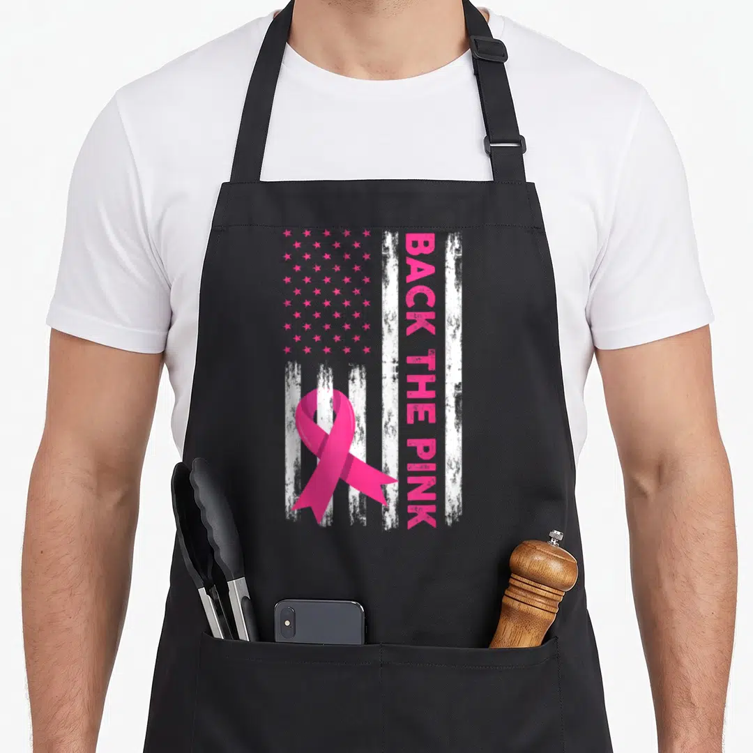 Retro breast cancer awareness aprons - Pink ribbon over distressed US flag with vertical BACK THE PINK text — shown on a black cotton canvas apron against a white background
