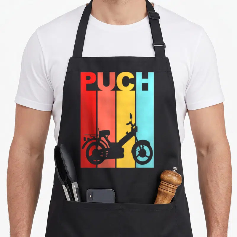 Puch scooter apron - Grey moped silhouette over red, orange, yellow, and light blue vertical stripes with PUCH text — shown on a black cotton canvas apron against a white background