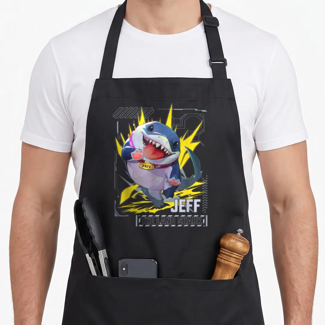 Rival super hero aprons - Cartoon blue shark with purple collar over yellow shapes labeled Jeff The Land Shark — shown on a black cotton canvas apron against a white background