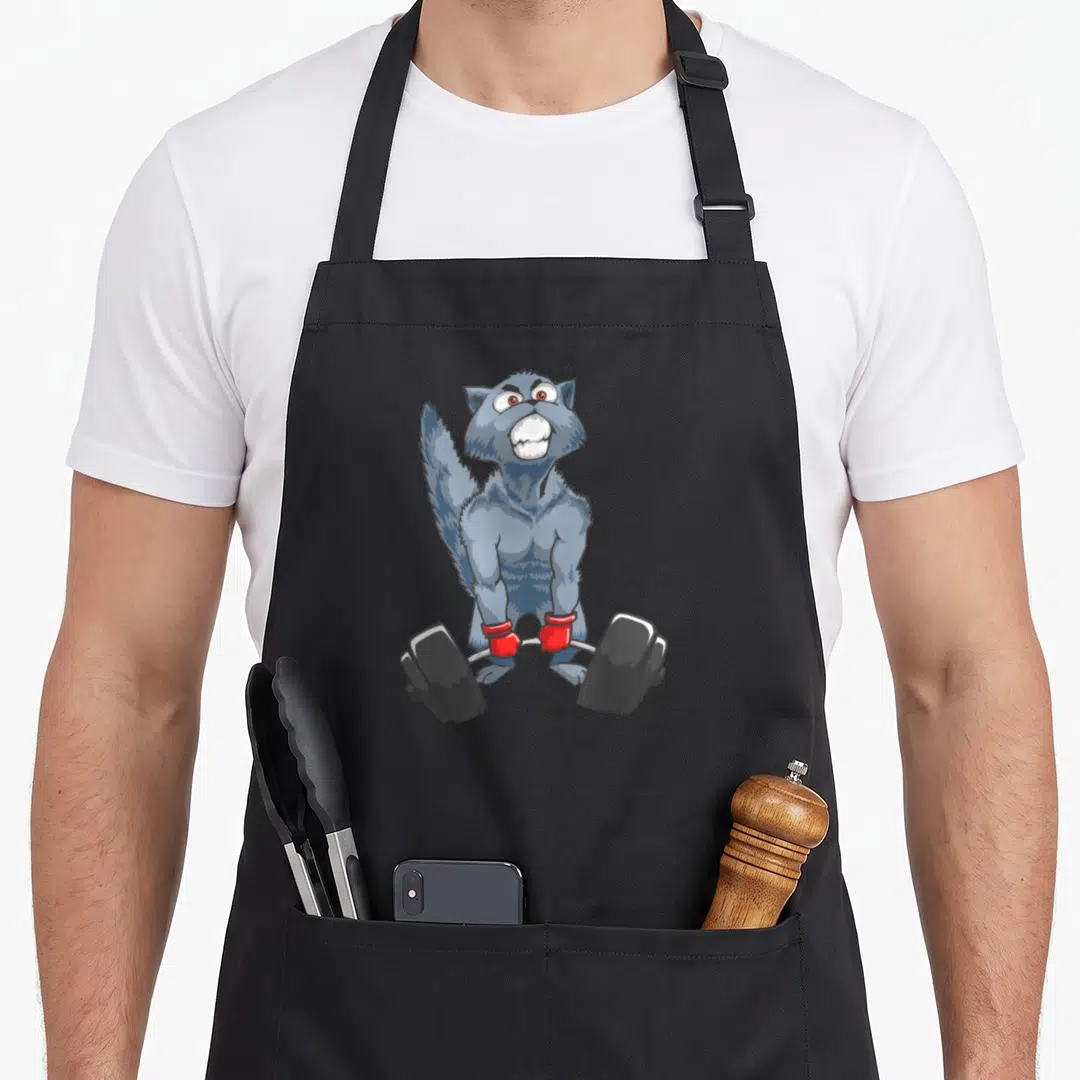 Deadlifting cat apron - Grey cartoon cat standing and lifting a barbell with red wrist wraps and black plates — shown on a black cotton canvas apron against a white background