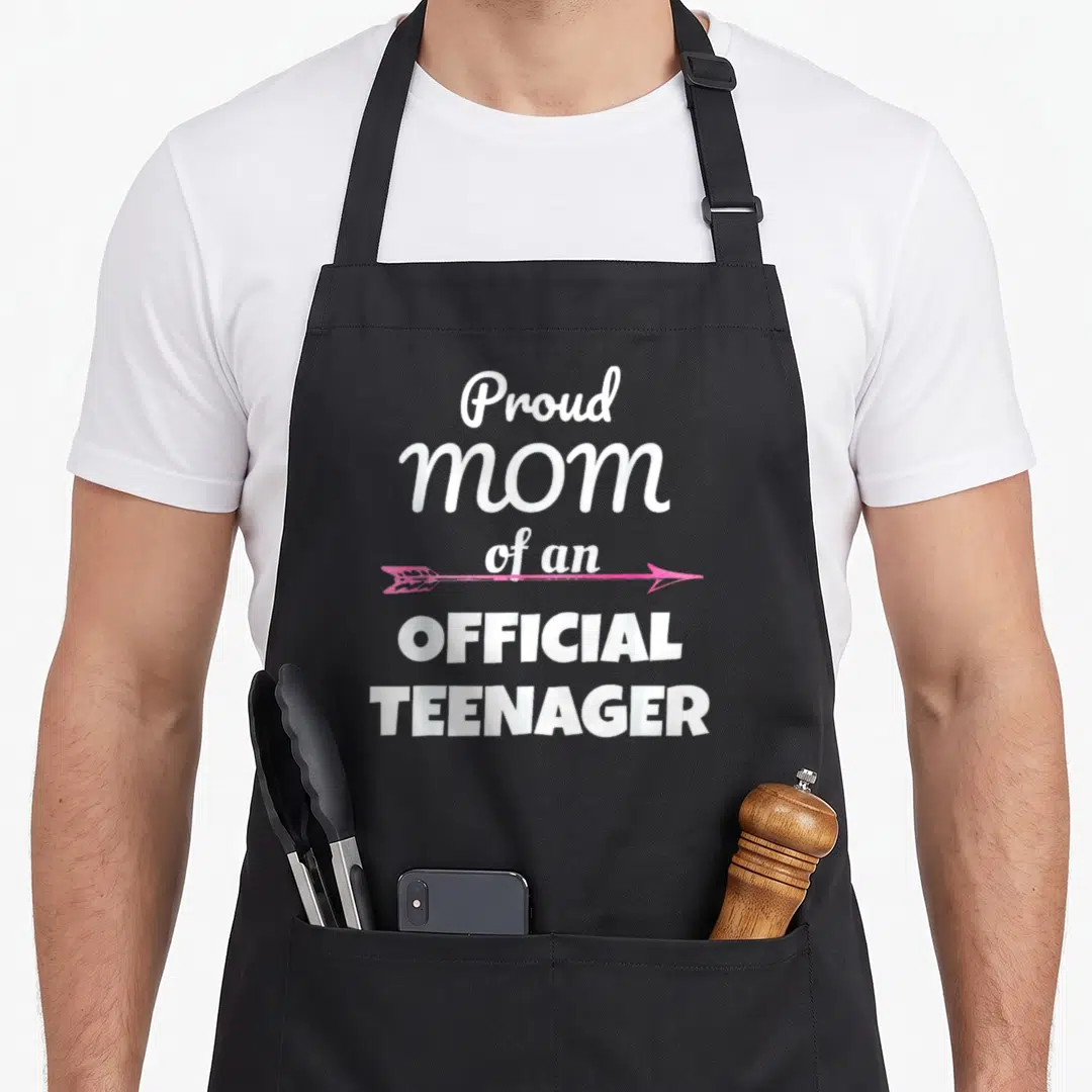 13th mother's apron - White stacked text reading Proud mom of an official teenager with a pink arrow — shown on a black cotton canvas apron against a white background