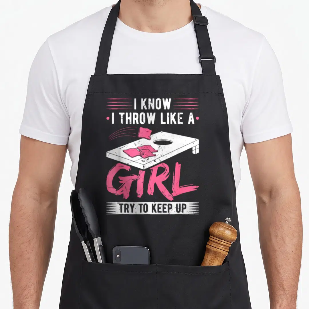 Throw game aprons - Distressed white and pink cornhole board with bean bags and stacked text reading I KNOW I THROW — shown on a black cotton canvas apron against a white background