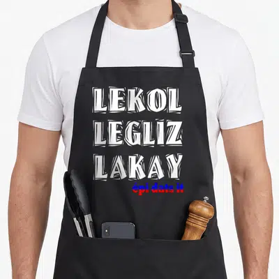 Haitian creole apron - Lekol Legliz Lakay text in white blue and red stacked vertically — shown on a black cotton canvas apron against a white background