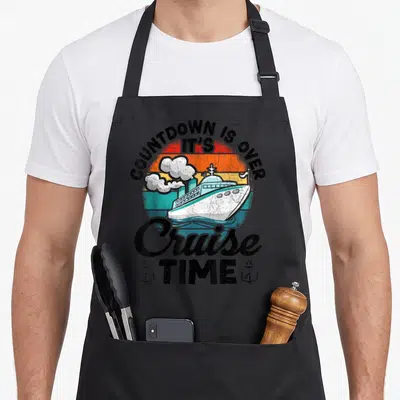 Funny cruise countdown apron - Retro ship graphic with arched text COUNTDOWN IS OVER IT'S Cruise TIME and two anchors — shown on a black cotton canvas apron against a white background