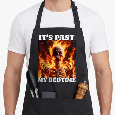 Past meme apron - Flaming skeleton between white text IT'S PAST and MY BEDTIME on orange and yellow fire — shown on a black cotton canvas apron against a white background