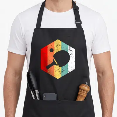 Pong tennis table apron - Grey ping pong paddle and ball silhouette over red orange yellow teal white striped hexagon — shown on a black cotton canvas apron against a white background