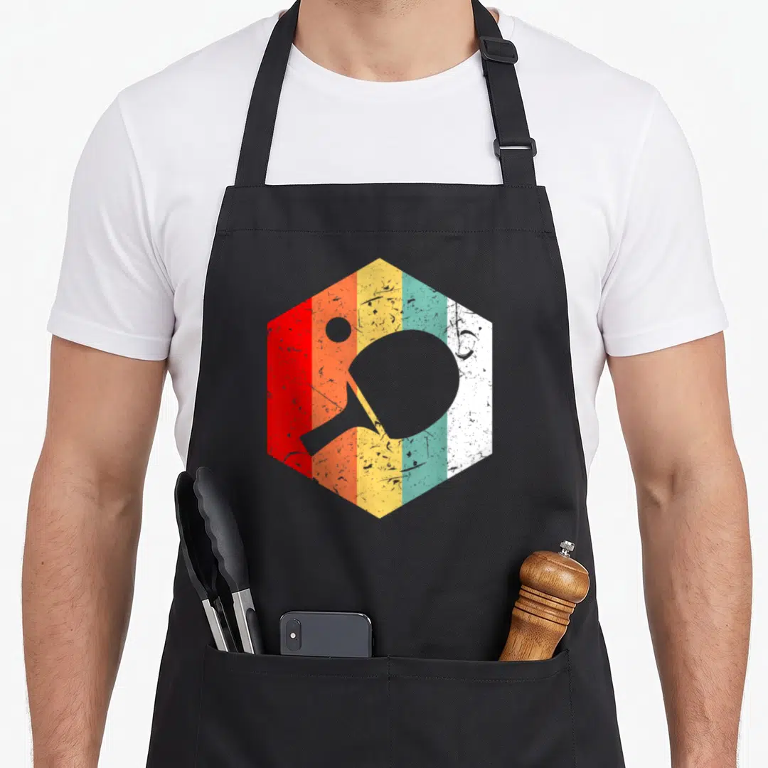 Pong tennis table apron - Grey ping pong paddle and ball silhouette over red orange yellow teal white striped hexagon — shown on a black cotton canvas apron against a white background