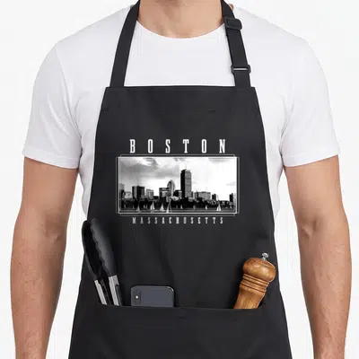 Boston pride apron - Black and white skyline photo framed by BOSTON and MASSACHUSETTS text — shown on a black cotton canvas apron against a white background