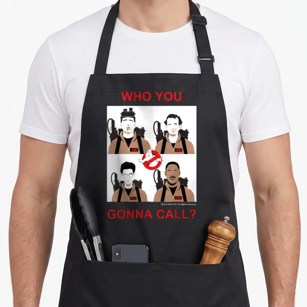 Panel novelty apron - Four Ghostbusters characters in brown jumpsuits surrounding a ghost logo with red text above — shown on a black cotton canvas apron against a white background