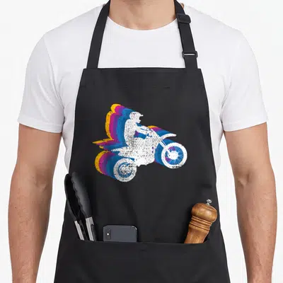 Motocross motorcross bike apron - White motocross rider silhouette with trailing blue magenta orange retro echoes — shown on a black cotton canvas apron against a white background