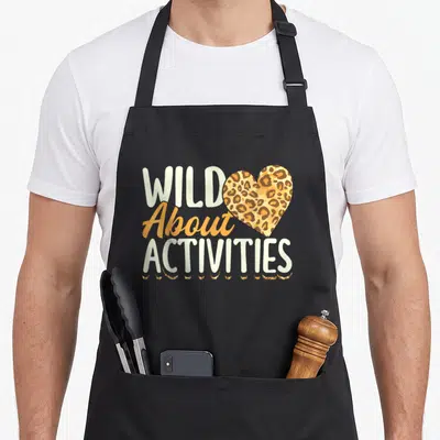 Assistant squad activity apron - Stacked Wild About Activities text with leopard heart and paw prints in orange brown — shown on a black cotton canvas apron against a white background