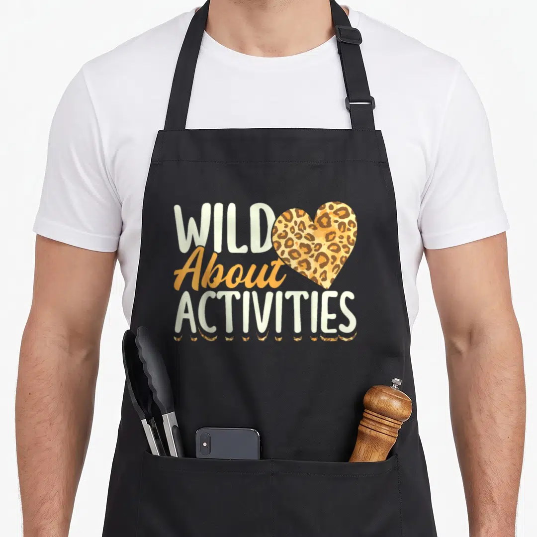 Assistant squad activity apron - Stacked Wild About Activities text with leopard heart and paw prints in orange brown — shown on a black cotton canvas apron against a white background