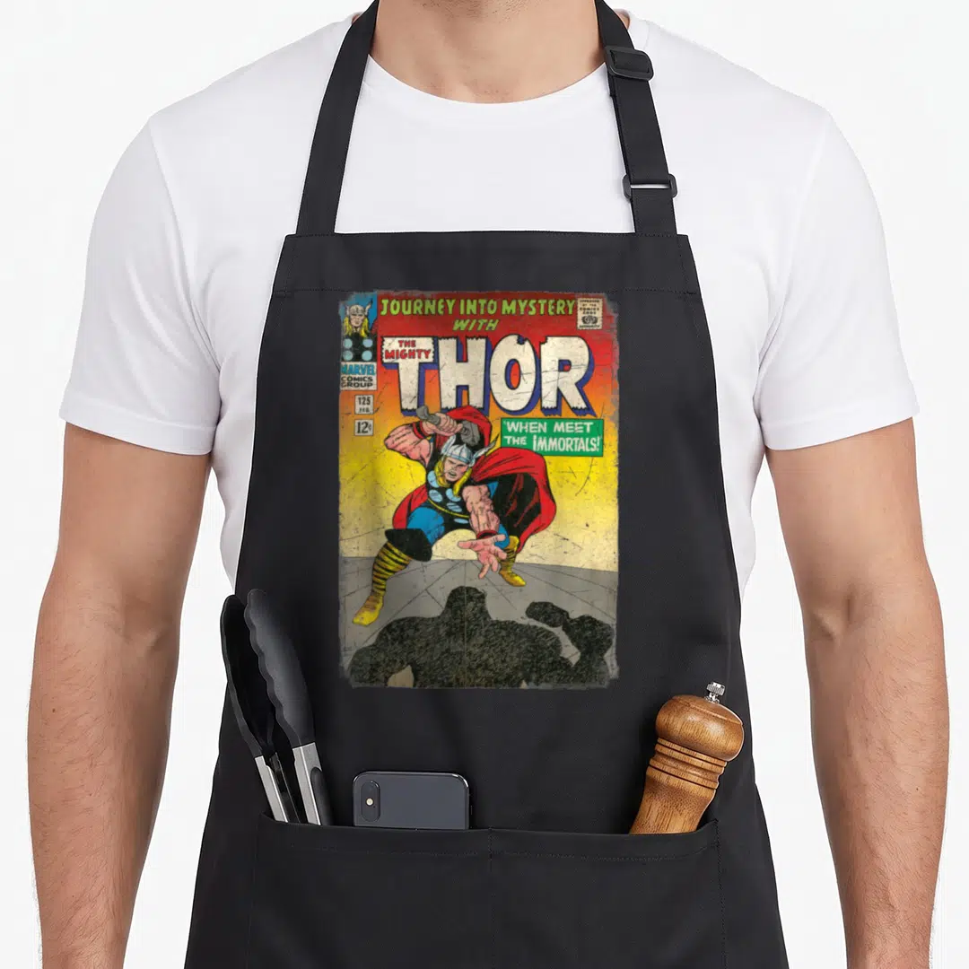 Mighty mystery apron - Retro Thor comic cover print with yellow and red colors and two front pockets — shown on a black cotton canvas apron against a white background