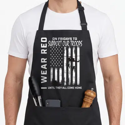 Military american flag apron - Distressed US flag with I WEAR RED text and military helicopter tank silhouettes — shown on a black cotton canvas apron against a white background