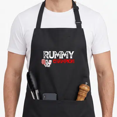 Rummy casino aprons - Rummy Champion text with poker chips and playing cards in white red black — shown on a black cotton canvas apron against a white background