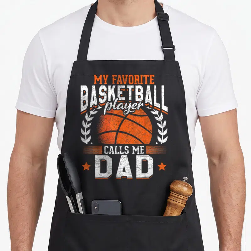 Funny call basketball player apron - Orange basketball with white laurel wreaths and distressed text reading My — shown on a black cotton canvas apron against a white background