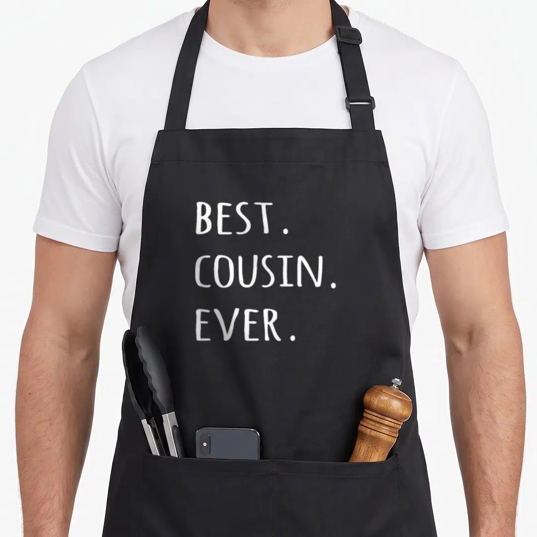 Cousin worlds greatest dad apron - White stacked text reading BEST. COUSIN. EVER on dark background — shown on a black cotton canvas apron against a white background