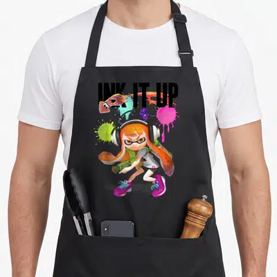 Ink squid lover apron - Inkling girl holding gun with INK IT UP text and leaping squid amidst orange pink green splats — shown on a black cotton canvas apron against a white background