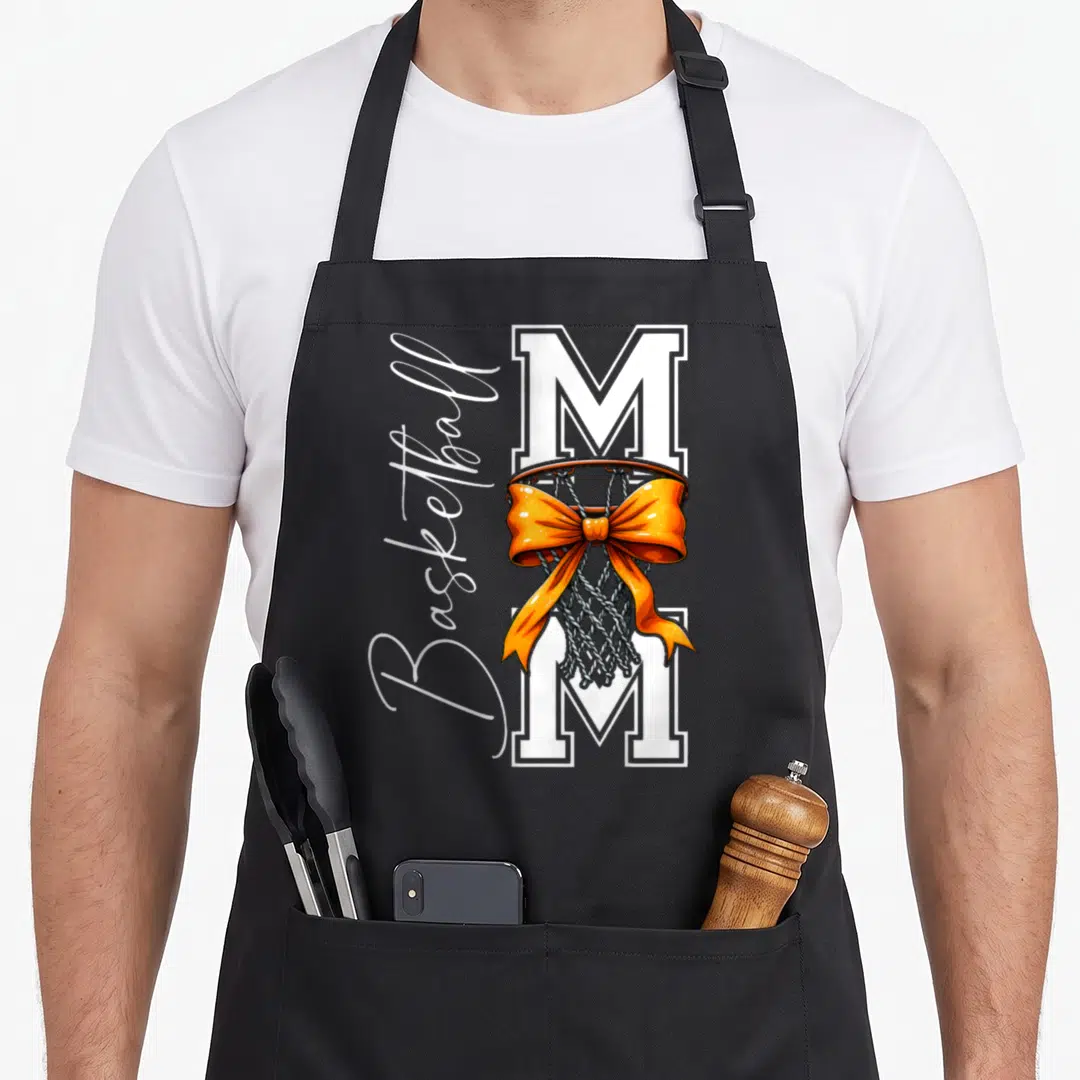Basketball game mother's day aprons - White M with orange bow on hoop and vertical Basketball script — shown on a black cotton canvas apron against a white background