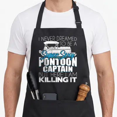 Captain pontooning boat apron - I Never Dreamed To Be A Super Sexy Pontoon Captain But Here I Am Killing It text — shown on a black cotton canvas apron against a white background