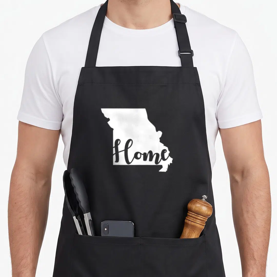 Funny missouri boy apron - White Missouri state map silhouette with grey Home script text — shown on a black cotton canvas apron against a white background