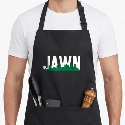 Local phillies apron - White JAWN text with green Philadelphia skyline silhouette overlay — shown on a black cotton canvas apron against a white background