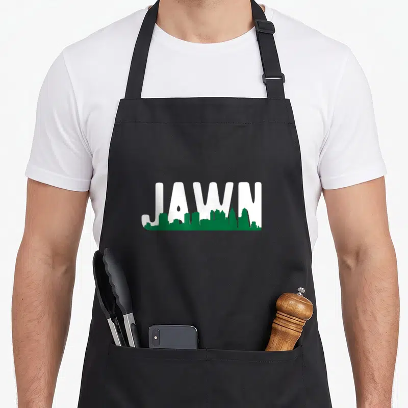 Local phillies apron - White JAWN text with green Philadelphia skyline silhouette overlay — shown on a black cotton canvas apron against a white background