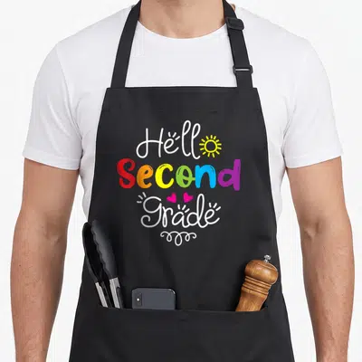 Hello second 2nd apron - Hello Second Grade rainbow text with yellow sun and two pink hearts — shown on a black cotton canvas apron against a white background