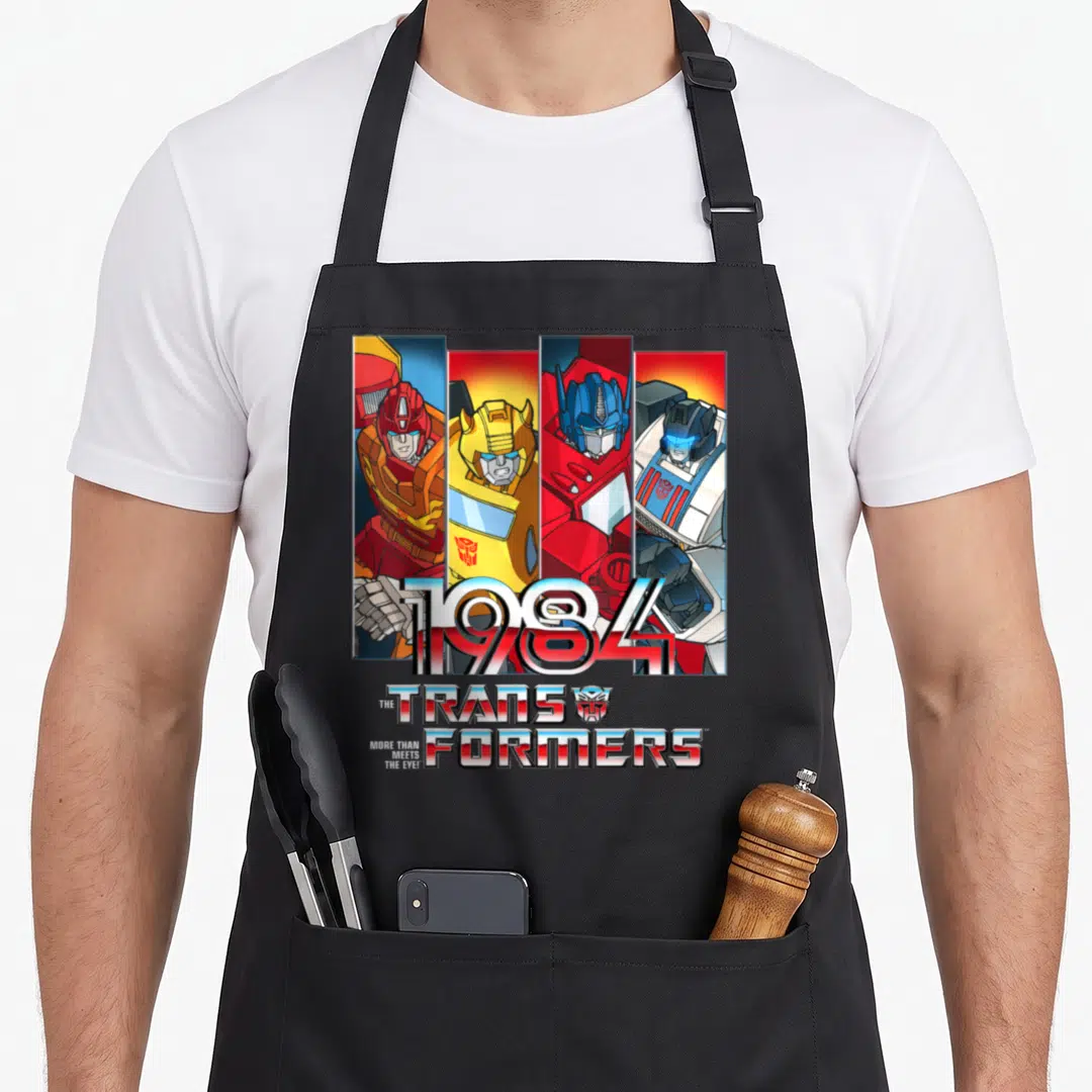 Autobot transformer apron - Four robots in vertical panels with 1984 text and Transformers logo — shown on a black cotton canvas apron against a white background
