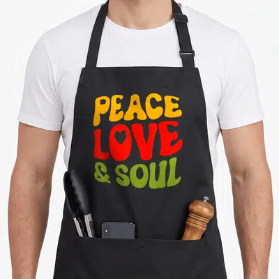 Groovy r aprons - Stacked text PEACE LOVE SOUL with heart in O colored orange red green — shown on a black cotton canvas apron against a white background