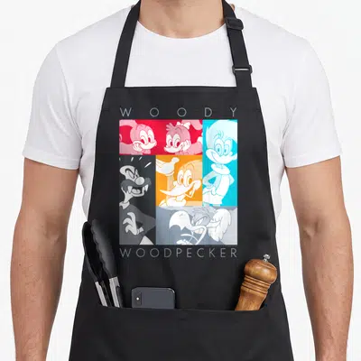 Panel woodpecker apron - Cartoon grid of Woody Woodpecker characters in red blue and orange blocks with WOODY — shown on a black cotton canvas apron against a white background