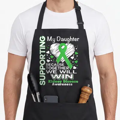 Supporting kidney disease awareness apron - Green ribbon over white heart with text supporting daughter kidney disease — shown on a black cotton canvas apron against a white background